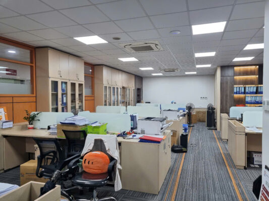 Hình ảnh không gian văn phòng hiện đại với nội thất tinh tế, ánh sáng tự nhiên, bàn làm việc màu be, thảm kẻ sọc, và trang trí hoa tạo cảm giác thoải mái và tập trung.