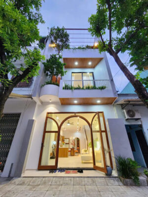 Hình ảnh ngôi nhà phố hiện đại với cửa kính lớn, khung gỗ nâu, cây xanh trên ban công và màu trắng thanh lịch